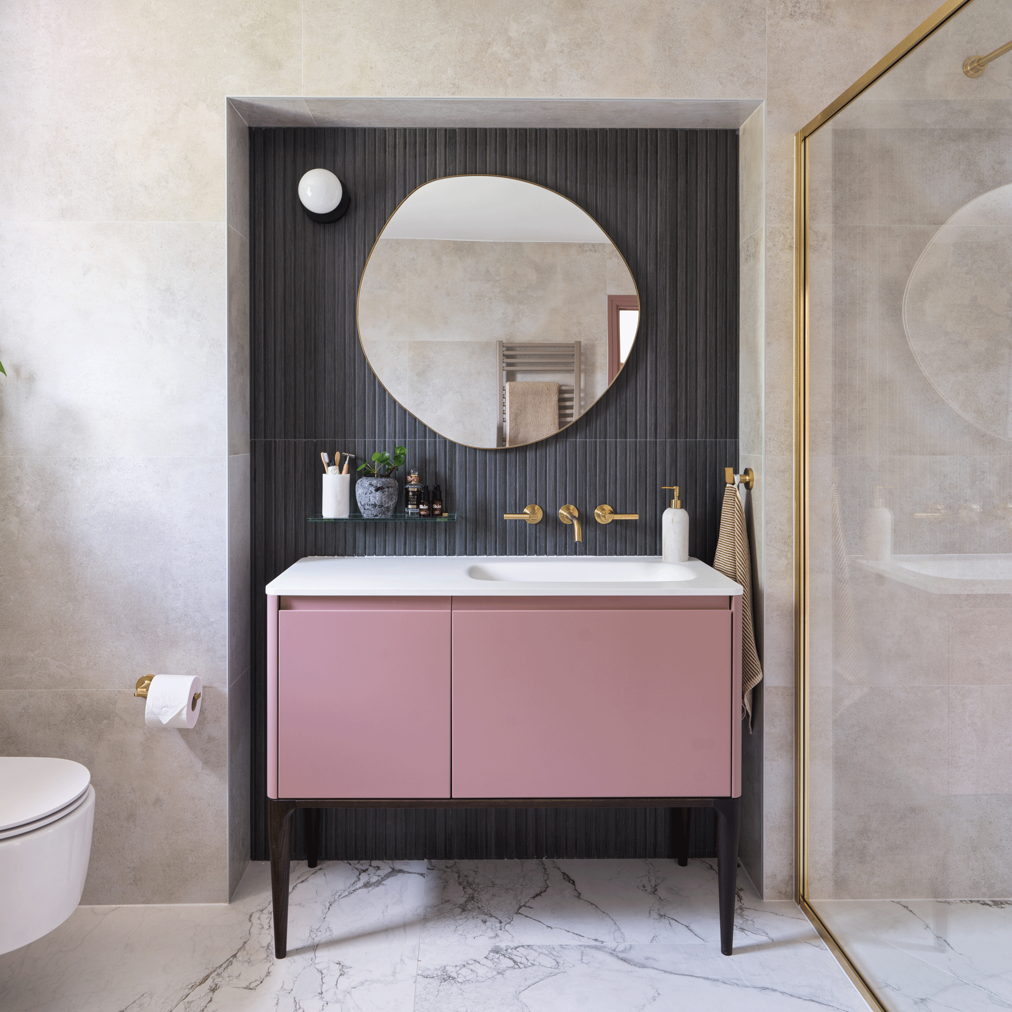 a bathroom with a modern pink vanity unit with sink with a charcoal tiled wall beside a large walk-in shower