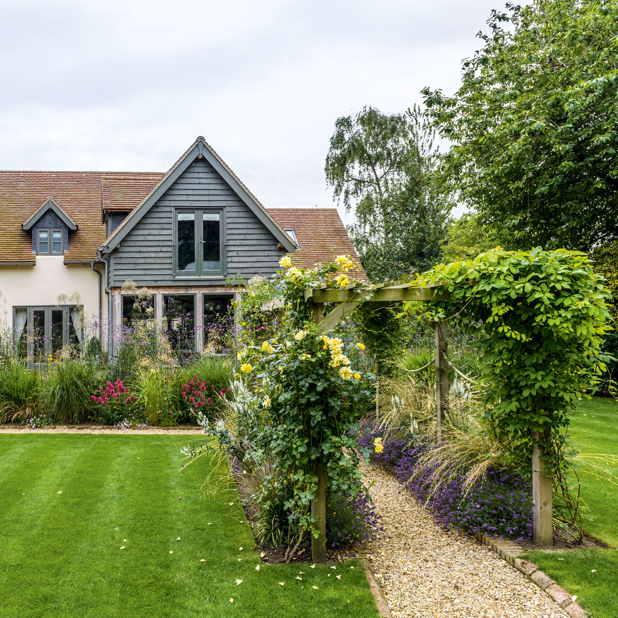 House with lawn and wooden arch with plants growing up over the arch