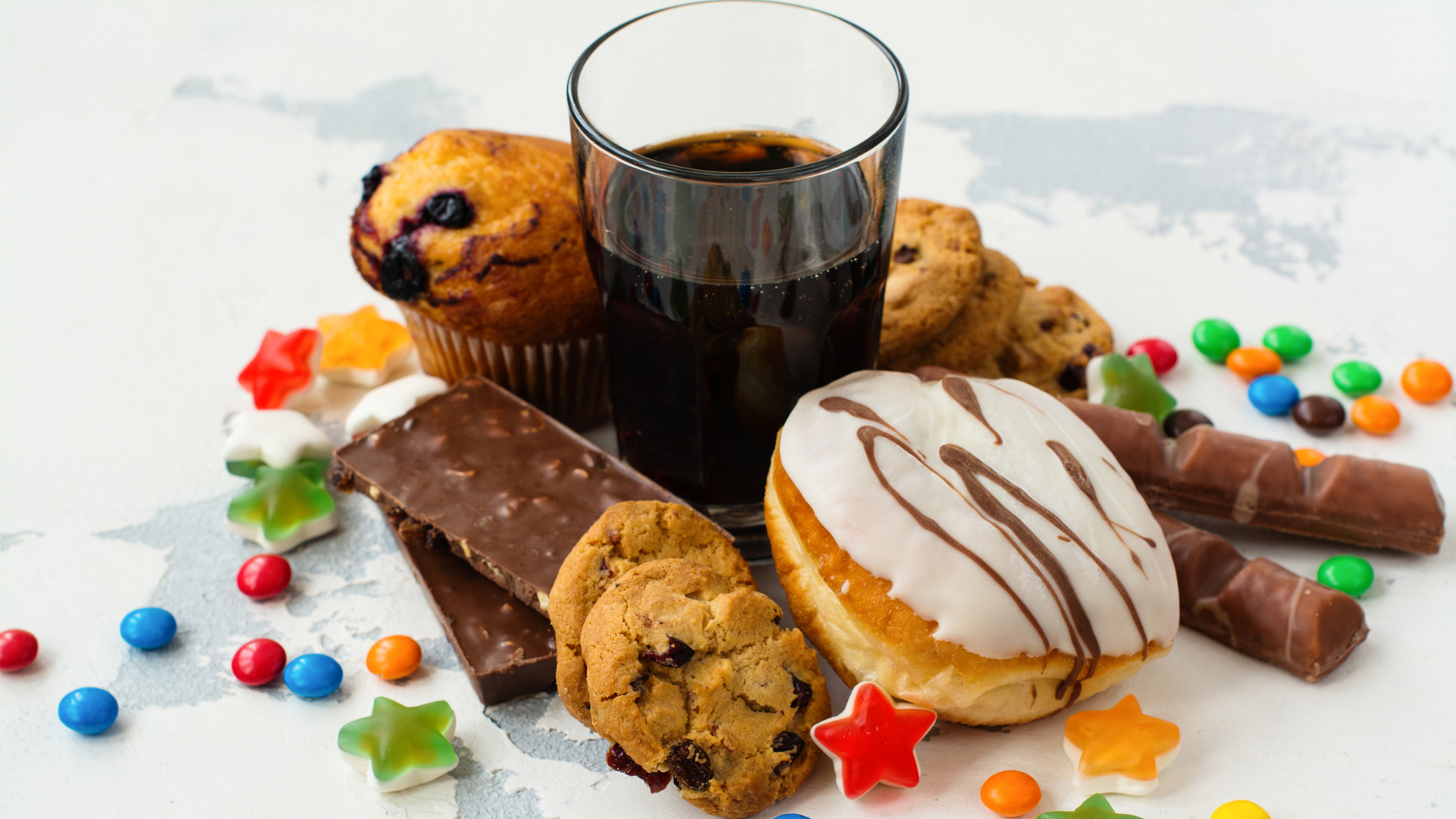 Das Bild zeigt verarbeitete Lebensmittel und einfache Kohlenhydrate, darunter Donuts, Soda, Kekse und Schokolade