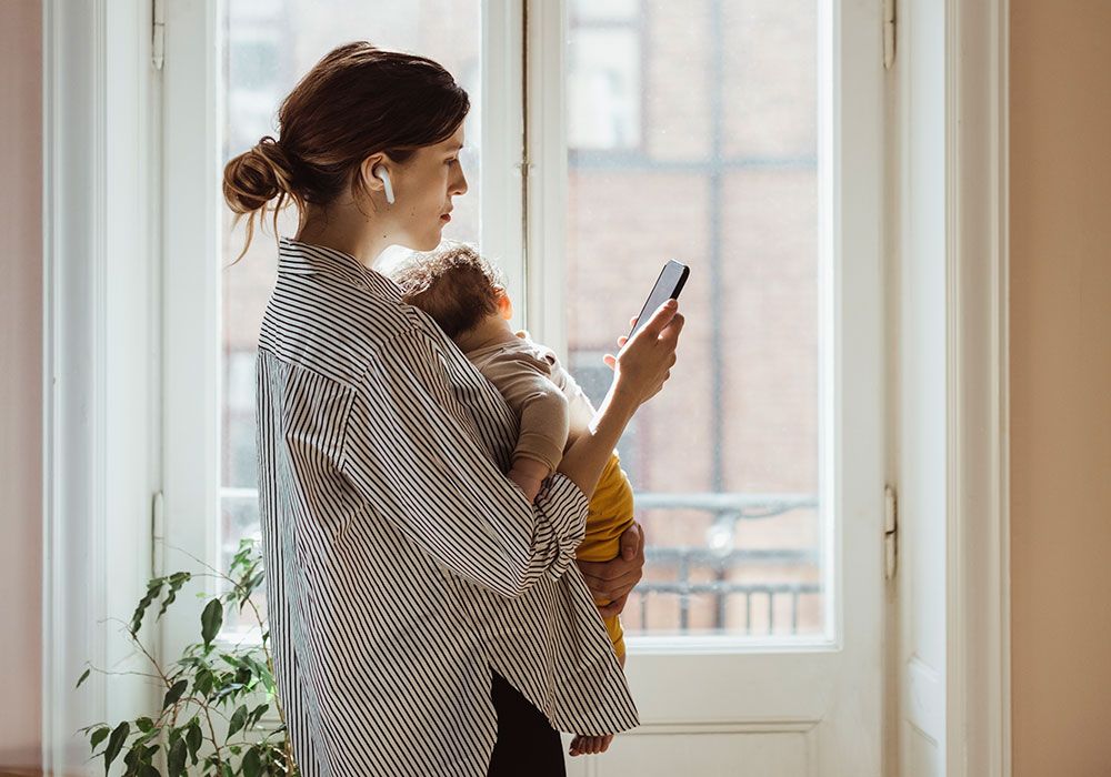 Multitasking mother carrying baby and looking at her phone