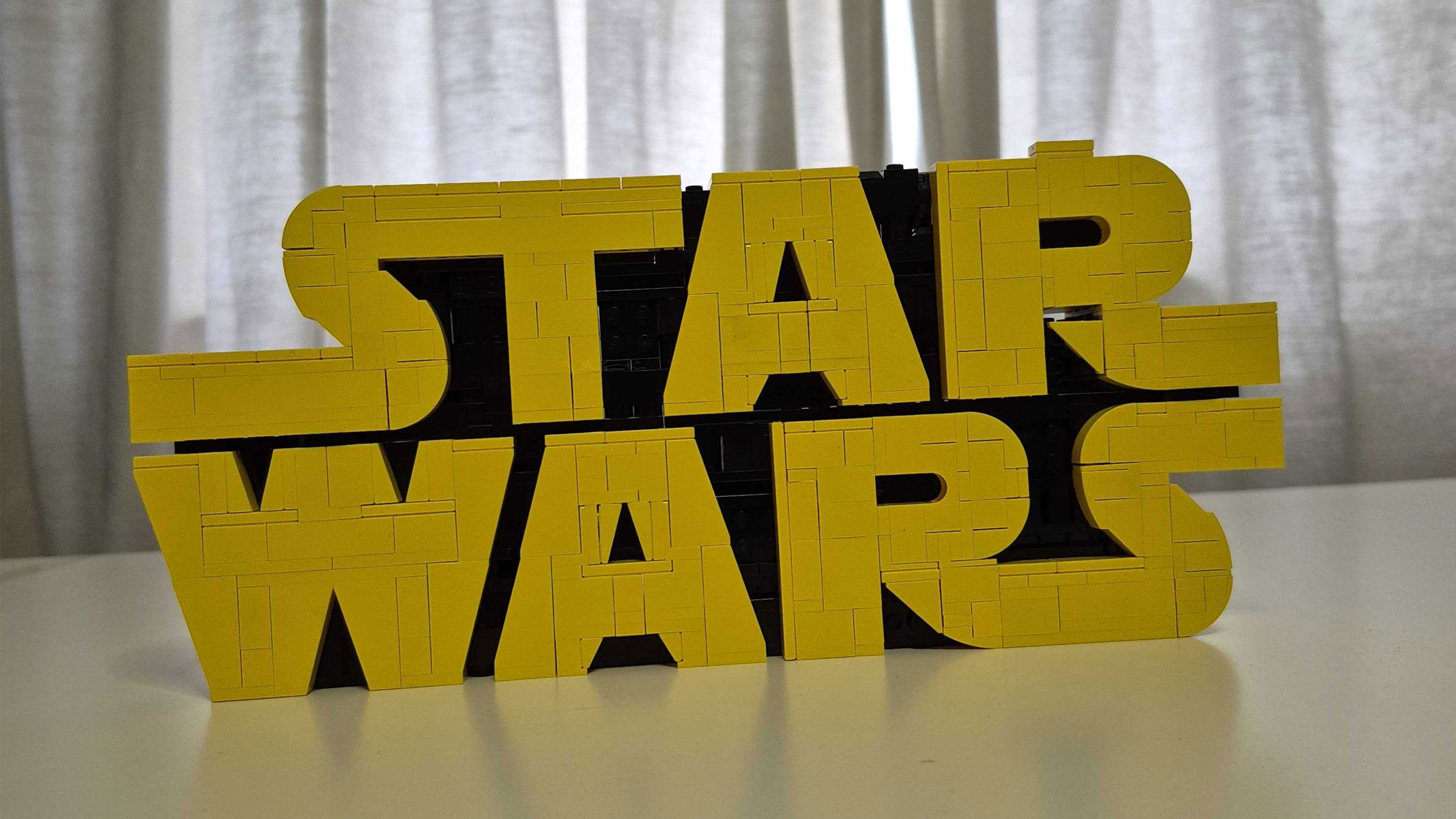 The Star Wars logo, which is the word "Star" above the word "Wars", in yellow lettering on a black background, in Lego form. 