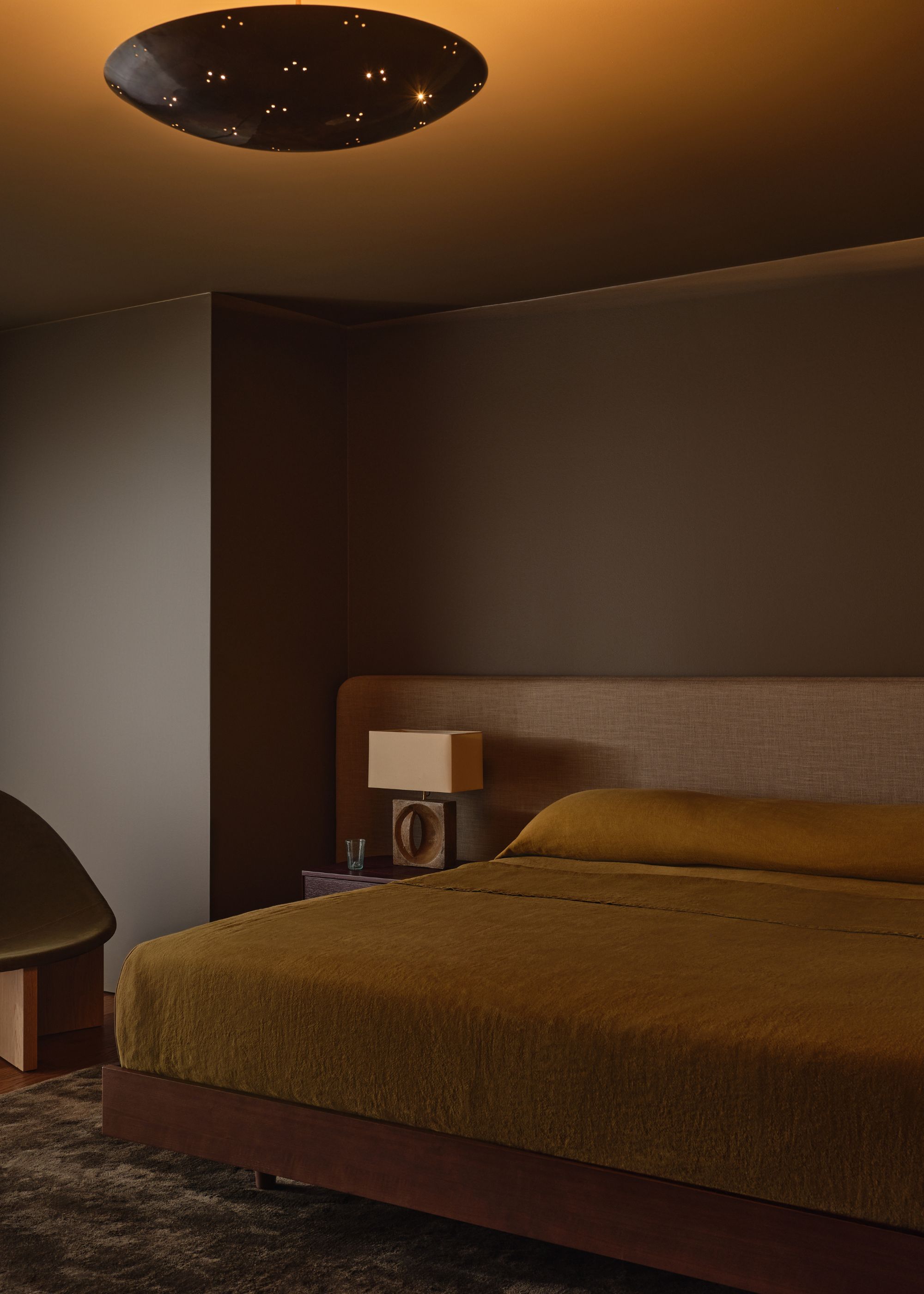 Modern minimalist bedroom with dark brown walls and dark ochre bedding.