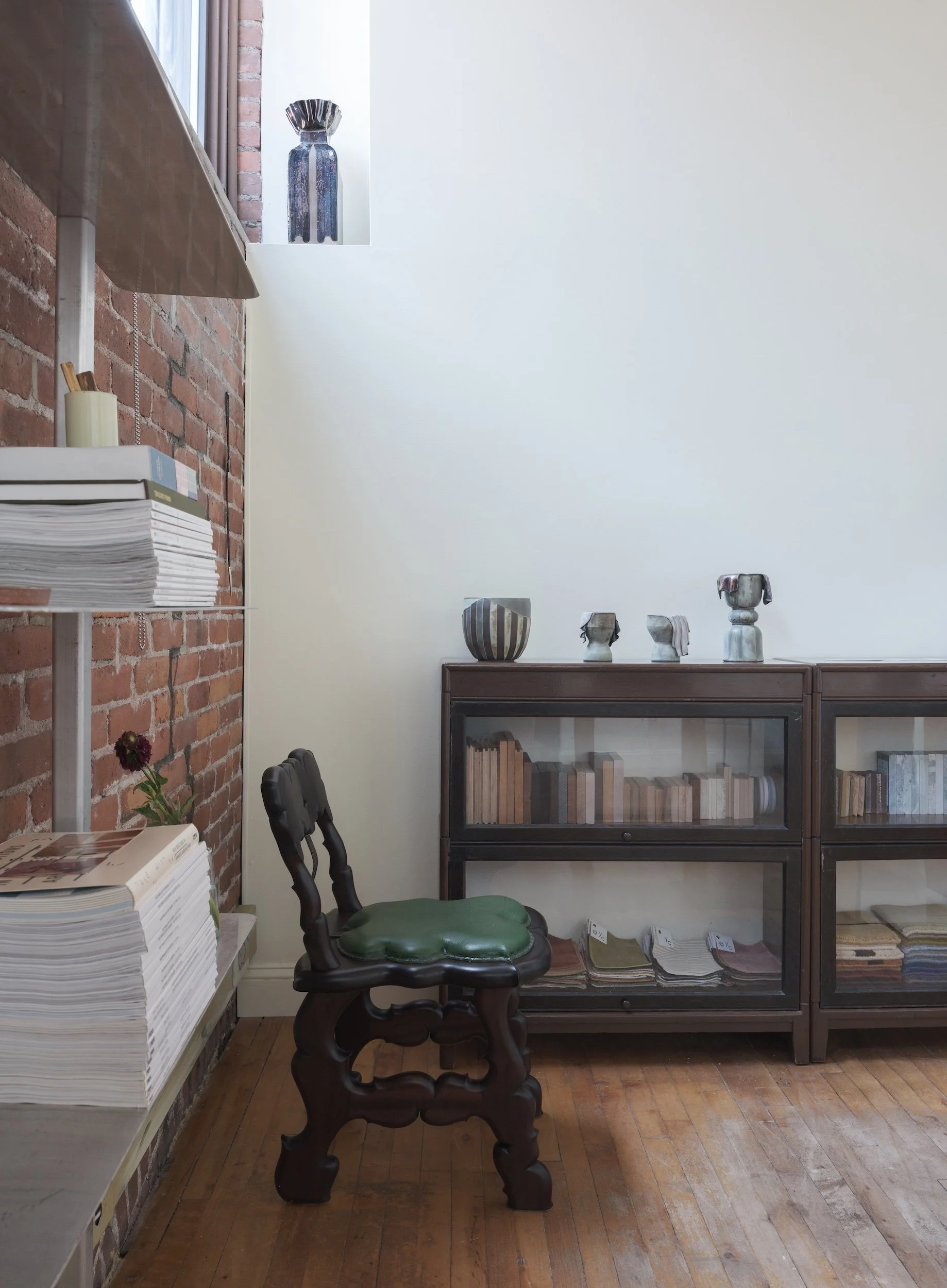 A gallery filled with books and antiques, decorated with wooden floors and red bricks and bathing in natural light.