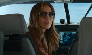 Jennifer Lopez sits in the pilot seat of a plane in her newest rom-com Office Romance.