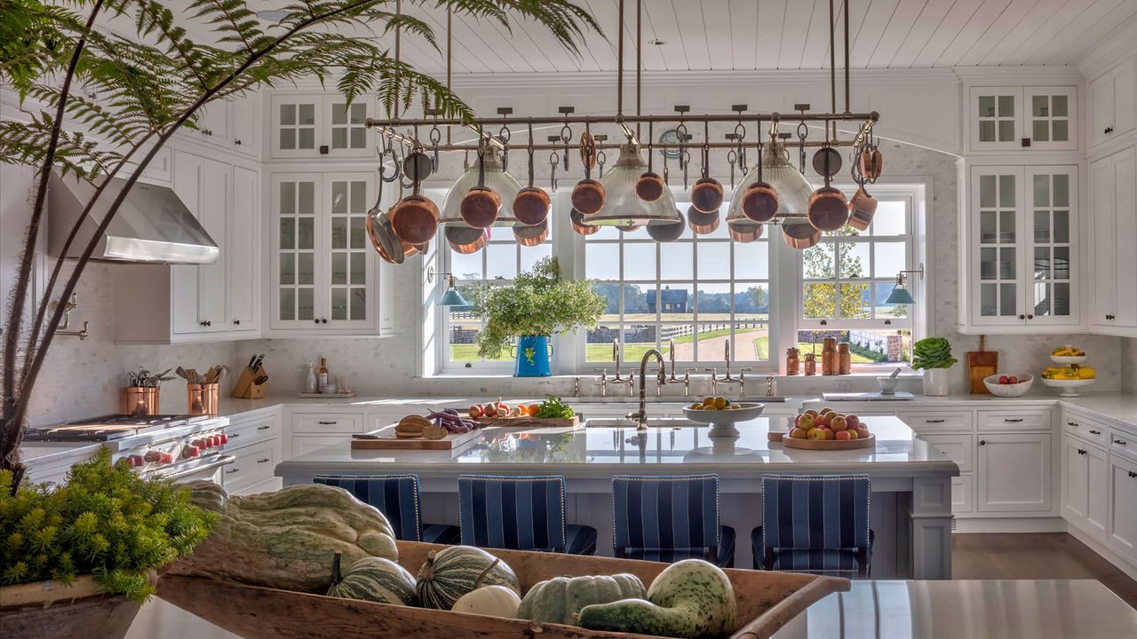 kitchen with copper pans hanging white units and two islands with blue striped bar stools 