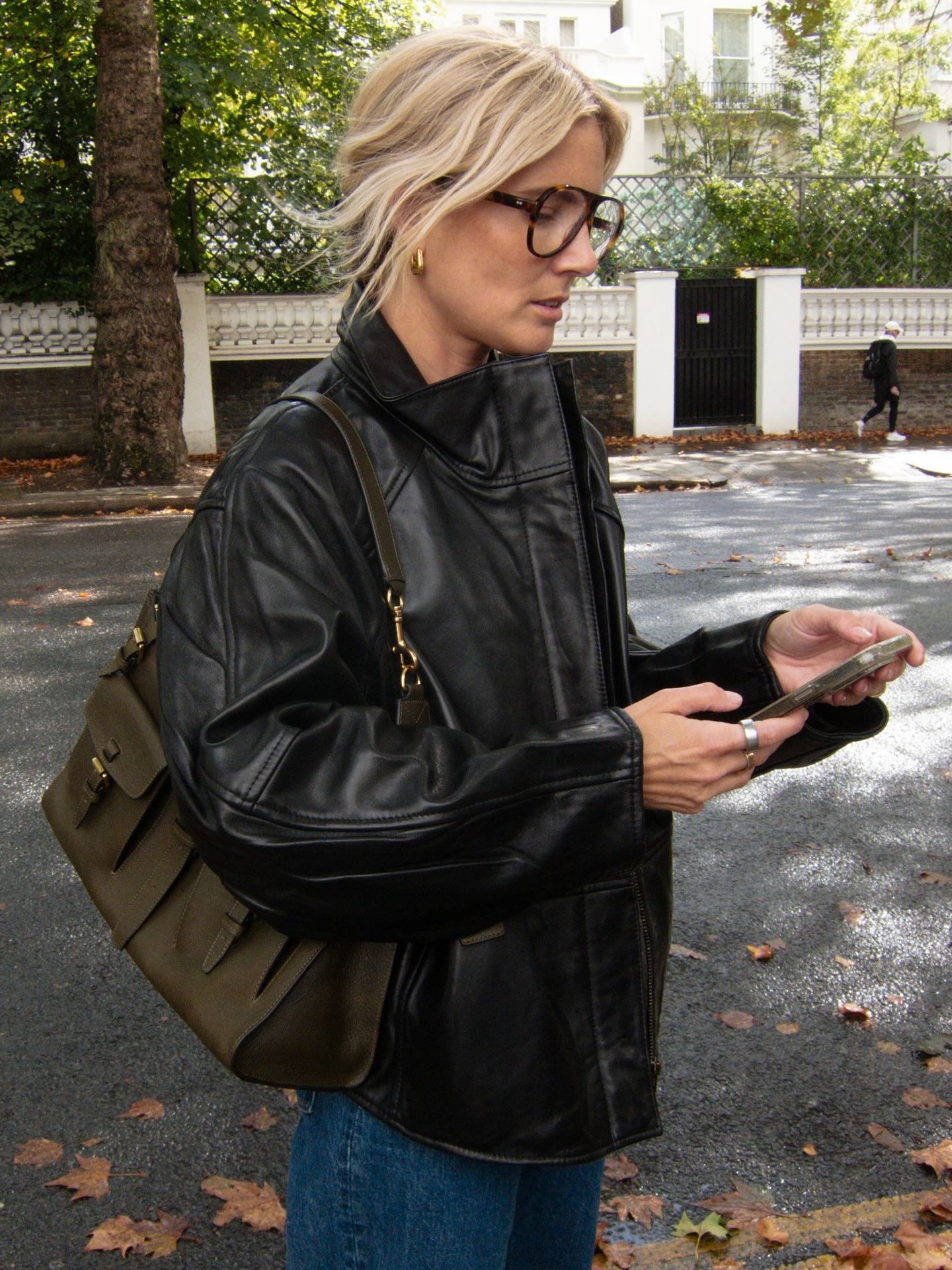 An image of an influencer in a black leather jacket and blue jeans carrying a dark green tote bag