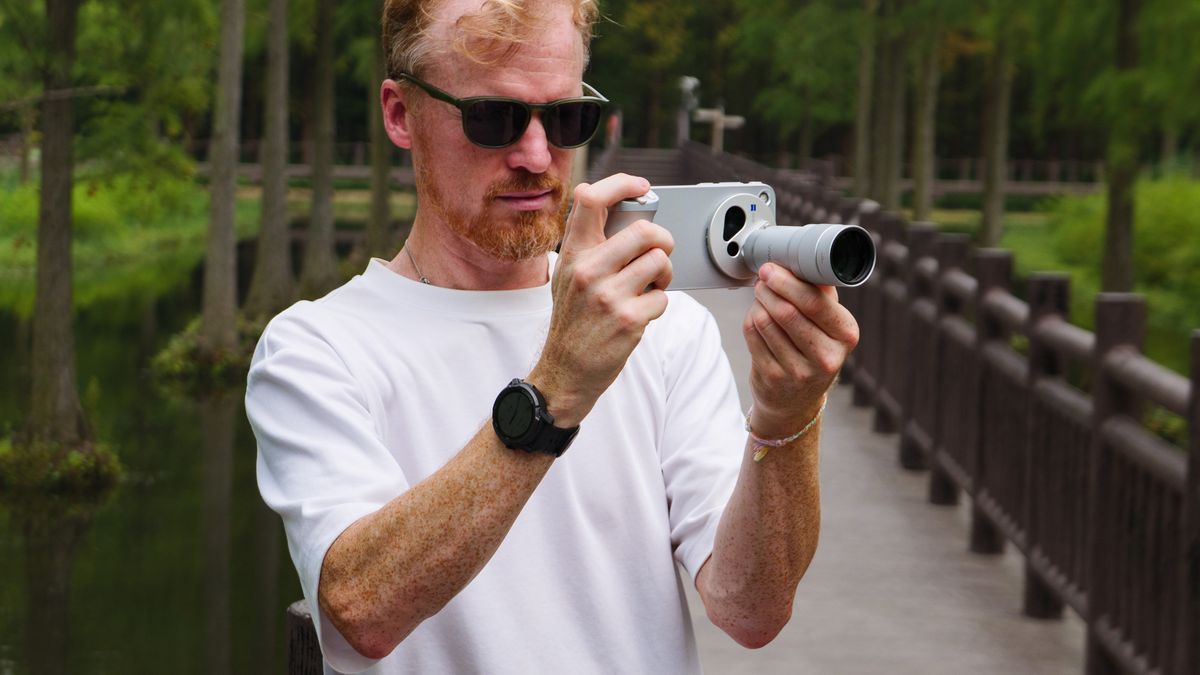 Tim Coleman, TechRadar's Cameras Editor, holding the Vivo X500 Pro Max phone with teleconverter lens attached, while stood on a wooden walkway in a birdlife reserve in Shanghai, China