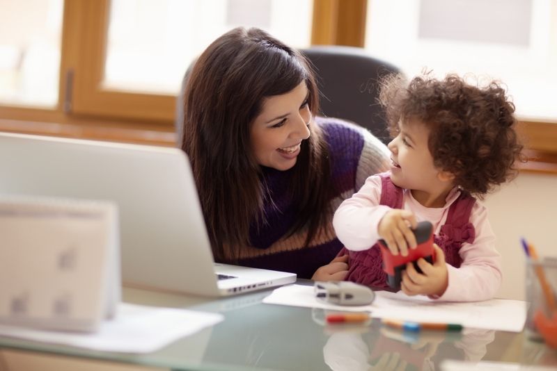 mom who is a businesswoman working at her laptop and playing with her baby girl.