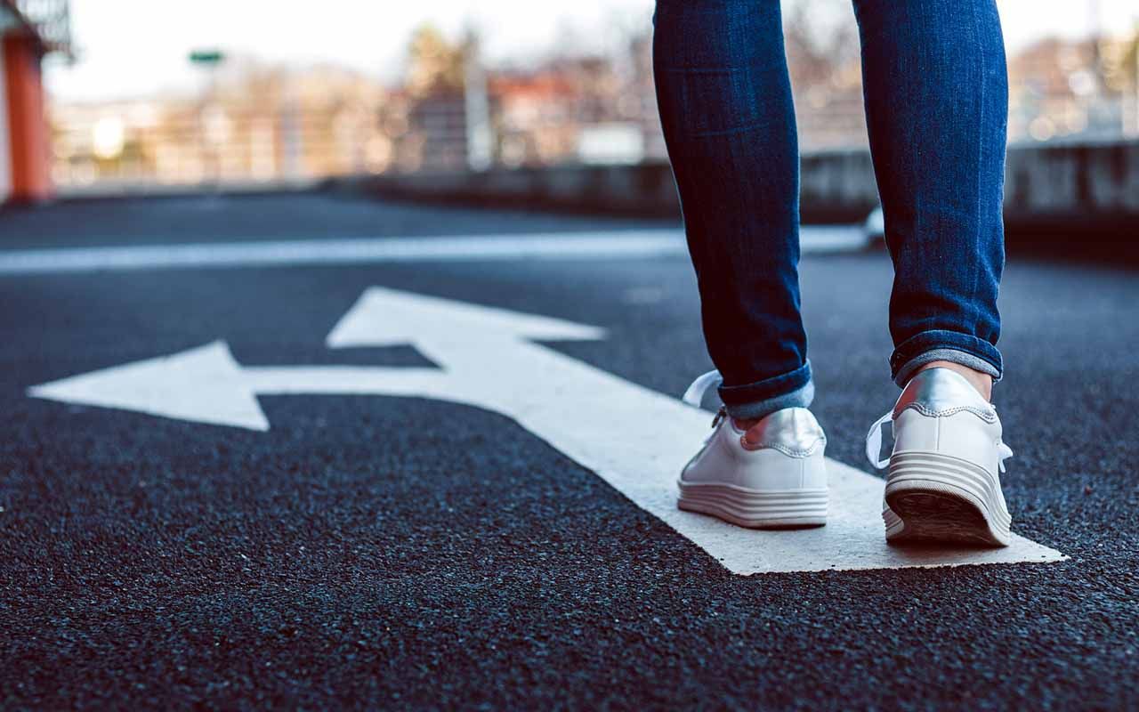 Female legs wearing jeans and white sneakers.