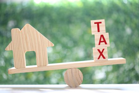 Model house and the word tax word balancing on a seesaw