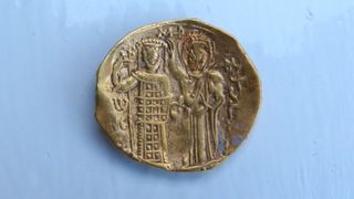 a close-up of a gold coin depicting two figures wearing extravagant clothing