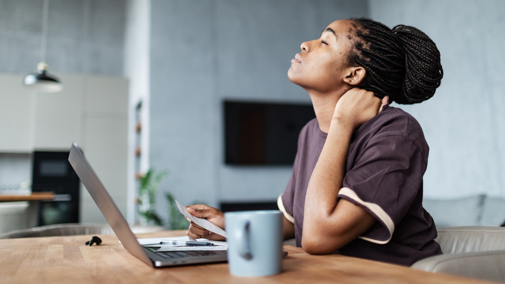 Woman sits in front of laptop and stretches her neck