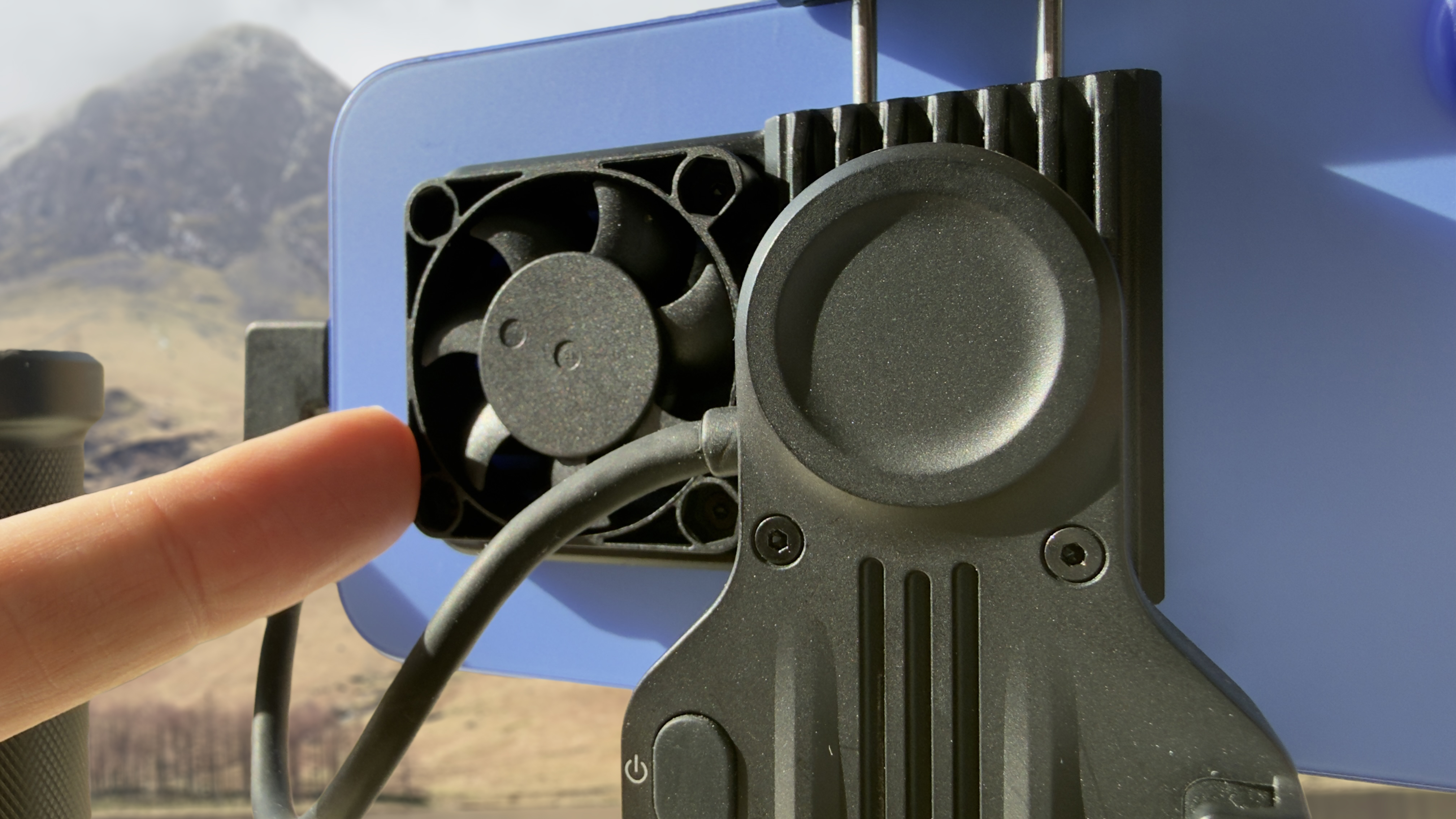 Close-up of an active cooling fan attached to the back of a smartphone mounted in a video rig to prevent overheating during filming.