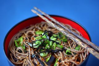 A bowl of buckwheat soba noodles with chopsticks on a blue background