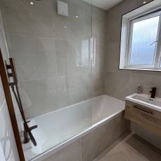 Small bathroom that has a fitted bath and floating vanity unit, all tiled in large-format beige tiles