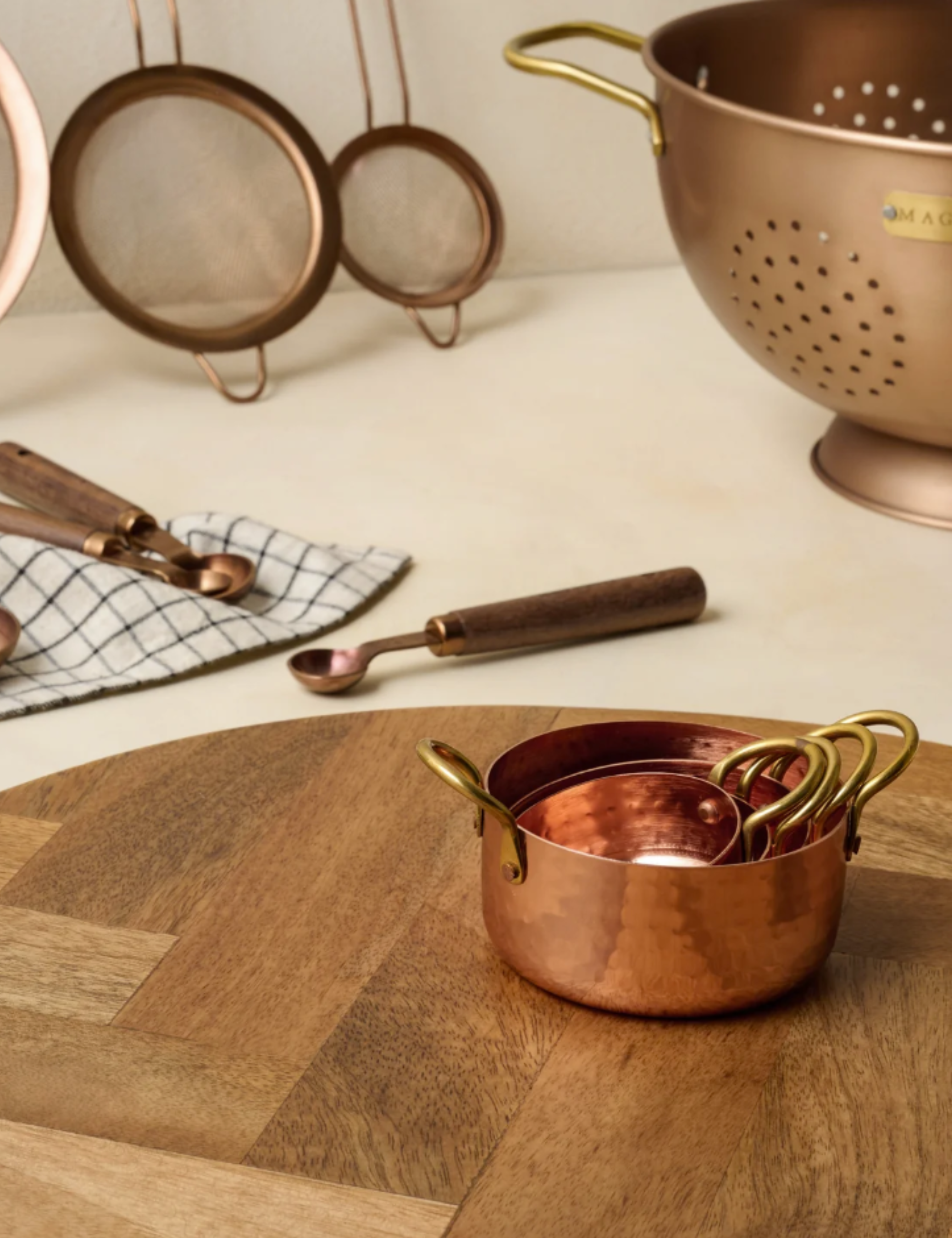 Herringbone wooden kitchen board styled with copper measuring cups, spoons, and strainers