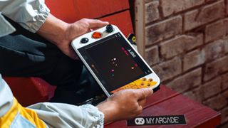 Player holding Atari GameStation Go sitting on red wooden bench.