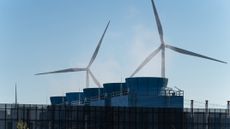 The heat vents of a data center in the foreground, with two large wind turbines visible in the background to show green renewable being used at a green data center.