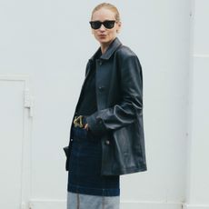 a woman wears a leather jacket, black top, and denim pencil skirt.