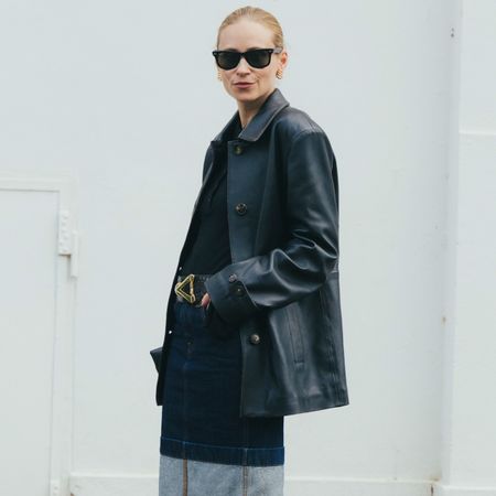 a woman wears a leather jacket, black top, and denim pencil skirt.