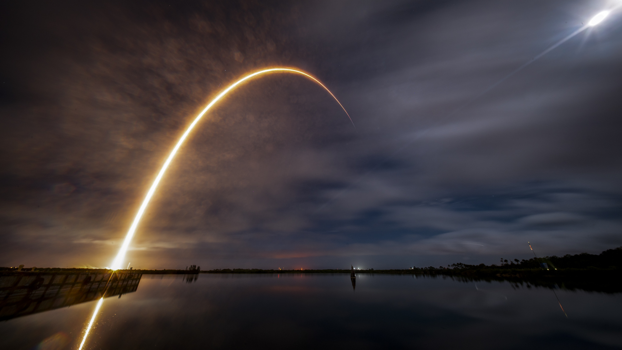 A thin light streaks into the cloudy night sky