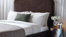 beige bedding on a brown velvet bed in a neutral room in front of a curtain wall