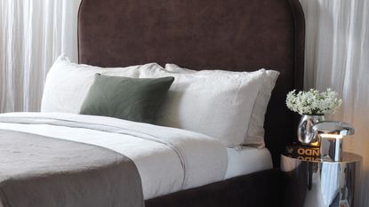 beige bedding on a brown velvet bed in a neutral room in front of a curtain wall
