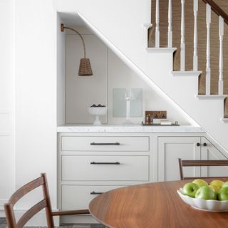 neutral kitchen cabinets under stairs and wooden dining table