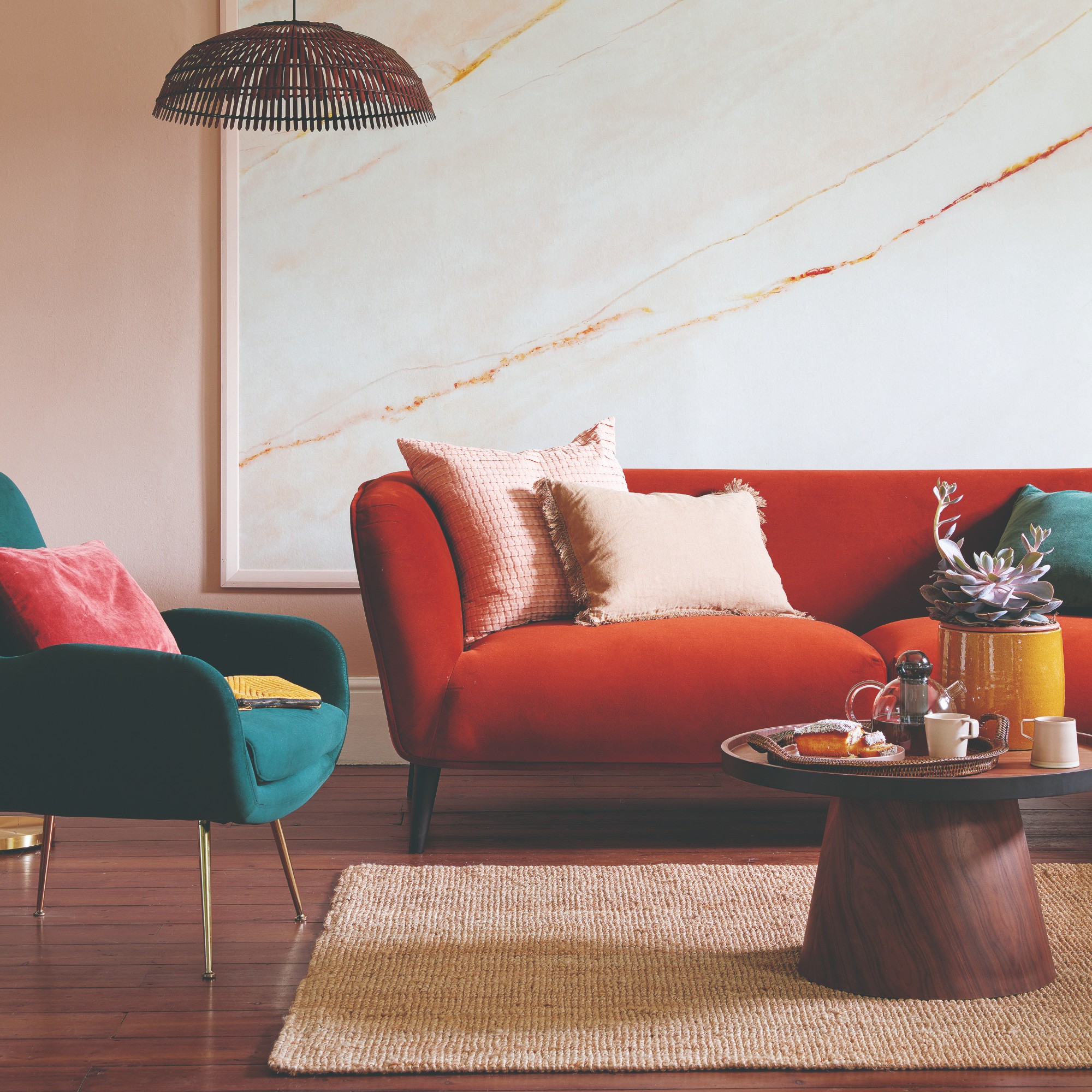 A pink-painted living room with a red velvet sofa, a beige natural texture rug and a round coffee table