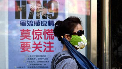 A woman wears a face mask as she walks past a poster showing how to avoid the H7N9 avian influenza virus, by a road in Beijing on April 24, 2013. International experts probing China's H7N9 bi