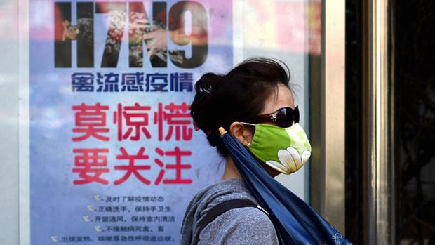 A woman wears a face mask as she walks past a poster showing how to avoid the H7N9 avian influenza virus, by a road in Beijing on April 24, 2013. International experts probing China&amp;#039;s H7N9 bi