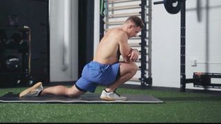 Athlete performing low runners lunge ankle stretch on exercise mat in the gym