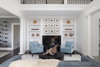 modern marble fireplace in living room with artwork above and flanked by two light blue velvet armchairs