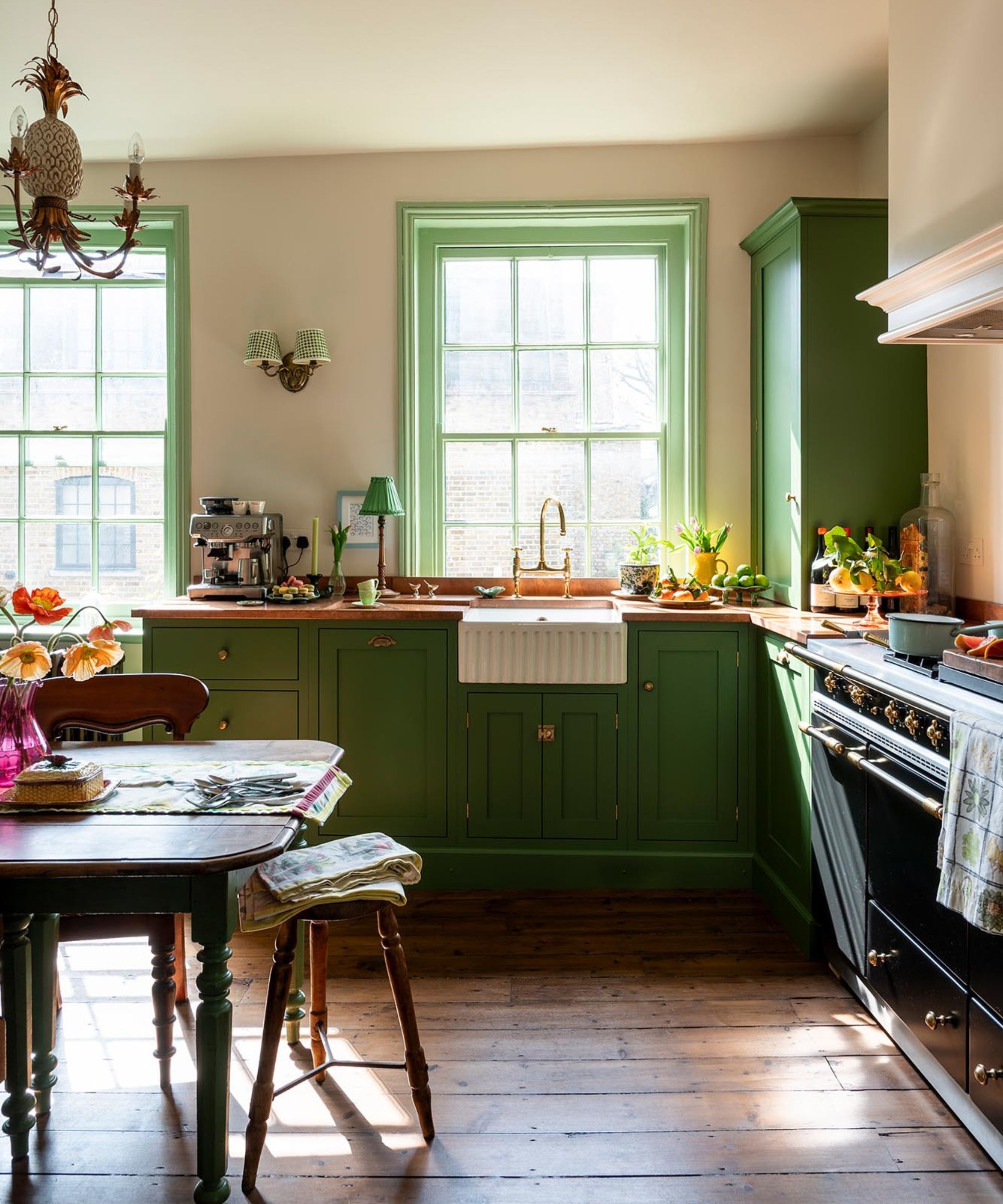 A small kitchen with green cabinets, copper countertops, a range cooker, and a vintage table and chairs set