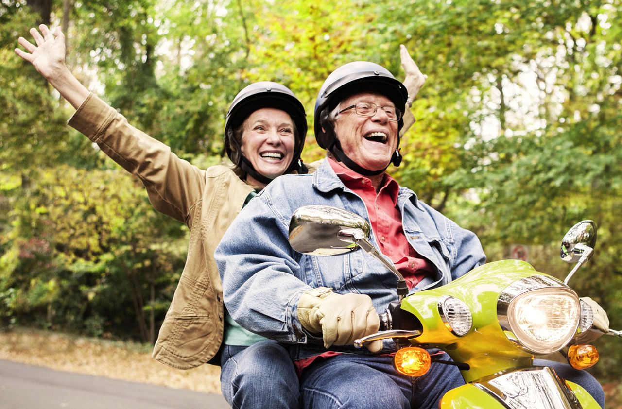 Happy senior couple traveling down road on motor scooter.