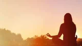 Woman meditating in front of a sunset