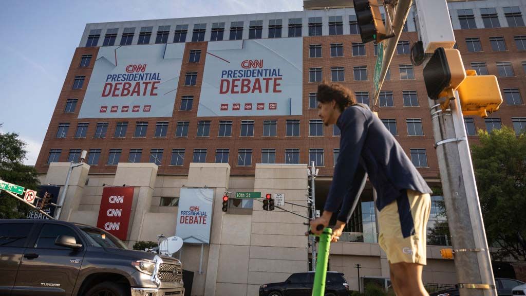 A man rides a scooter past banners outside of CNN studios ahead of the first presidential debate in Atlanta, Georgia on June 24, 2024. 