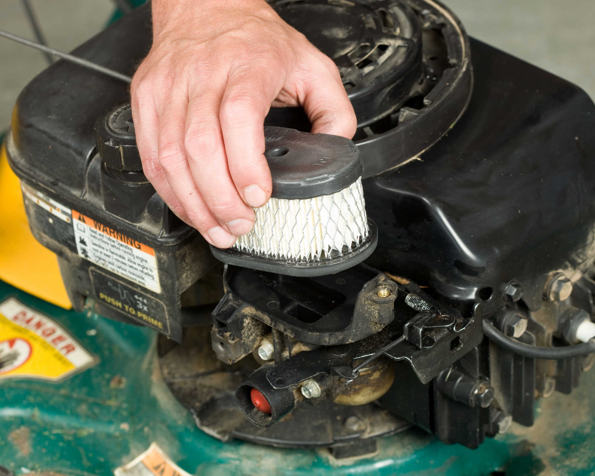 hand removing air filter from lawn mower