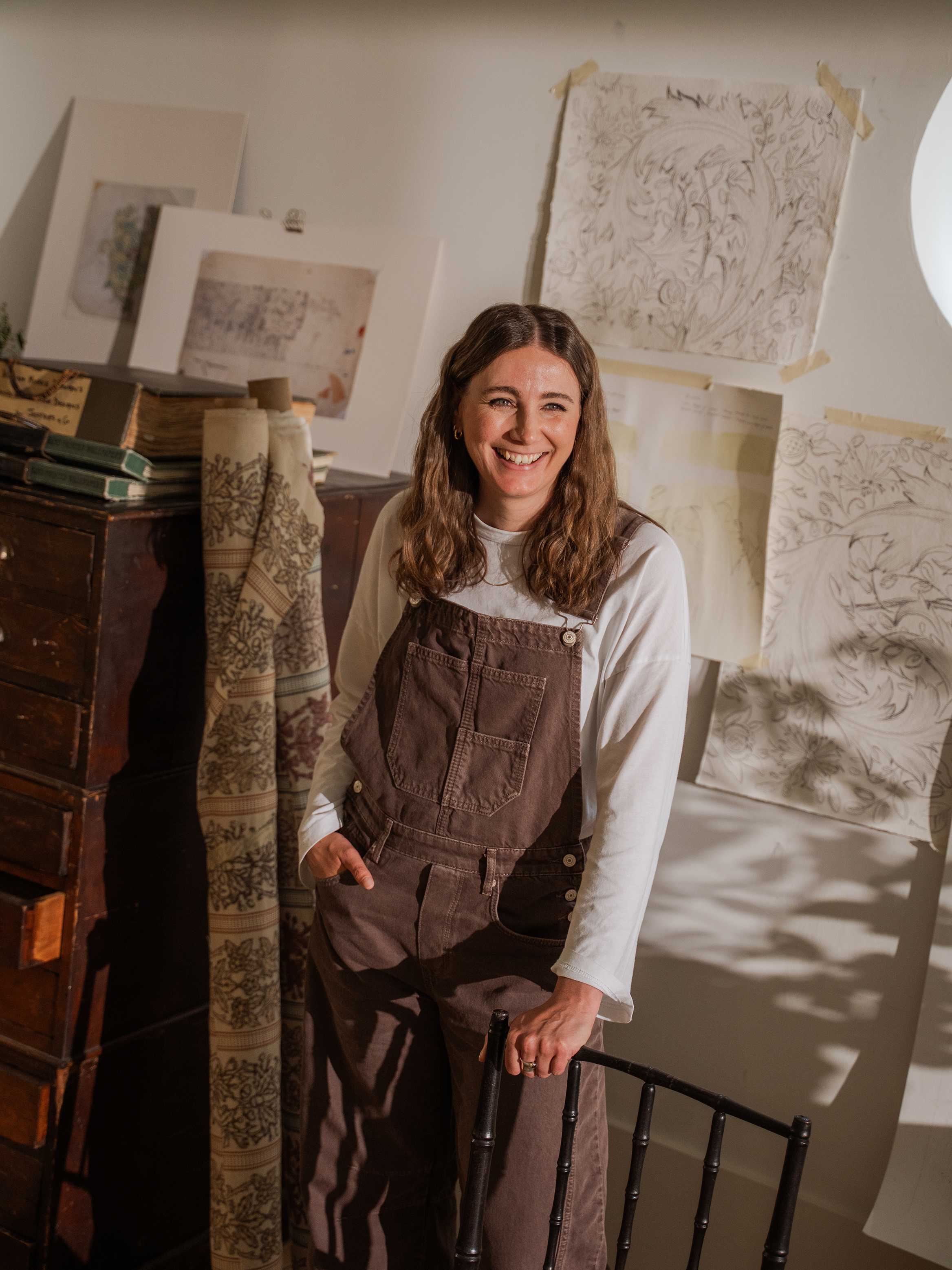 Jess Clayworth wears brown dungarees and stands in front of print and fabric samples