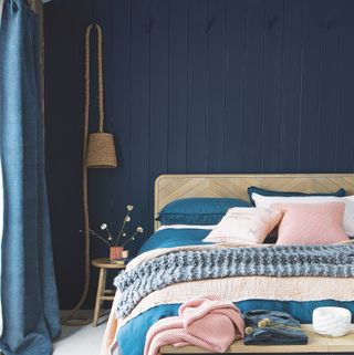 Bedroom with navy blue panelled walls, rope hanging wall light and wooden headboard