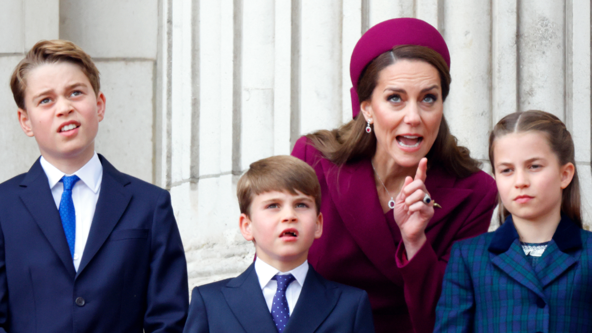 Kate Middleton looks stern while wearing a deep red coat dress and matching hat as she instructs children Prince George, Prince Louis, and Princess Charlotte