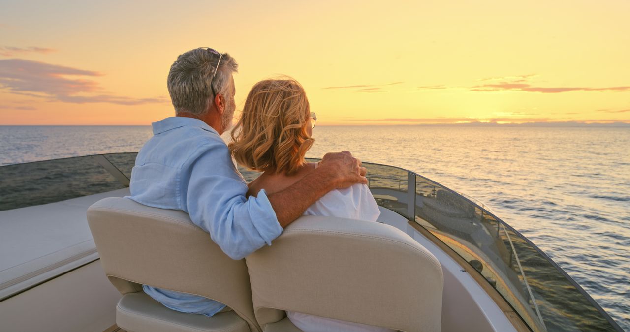 Senior couple driving luxury yacht in sea against sky.