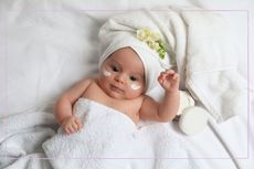 A baby wrapped in a towel with cream on its cheeks