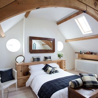 master bedroom with white wall and wooden beams with cushions on bed and mirror on wall
