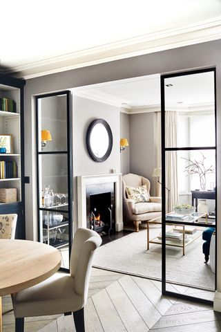 Grey living room-cum-dining room with parquet flooring and a crittall glass screen