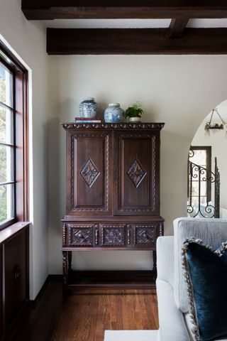 dark wood armoire with ornate carvings next to a white wall with edge of blue sofa in front