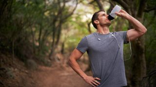 Man running in woods, pausing to consume energy drink