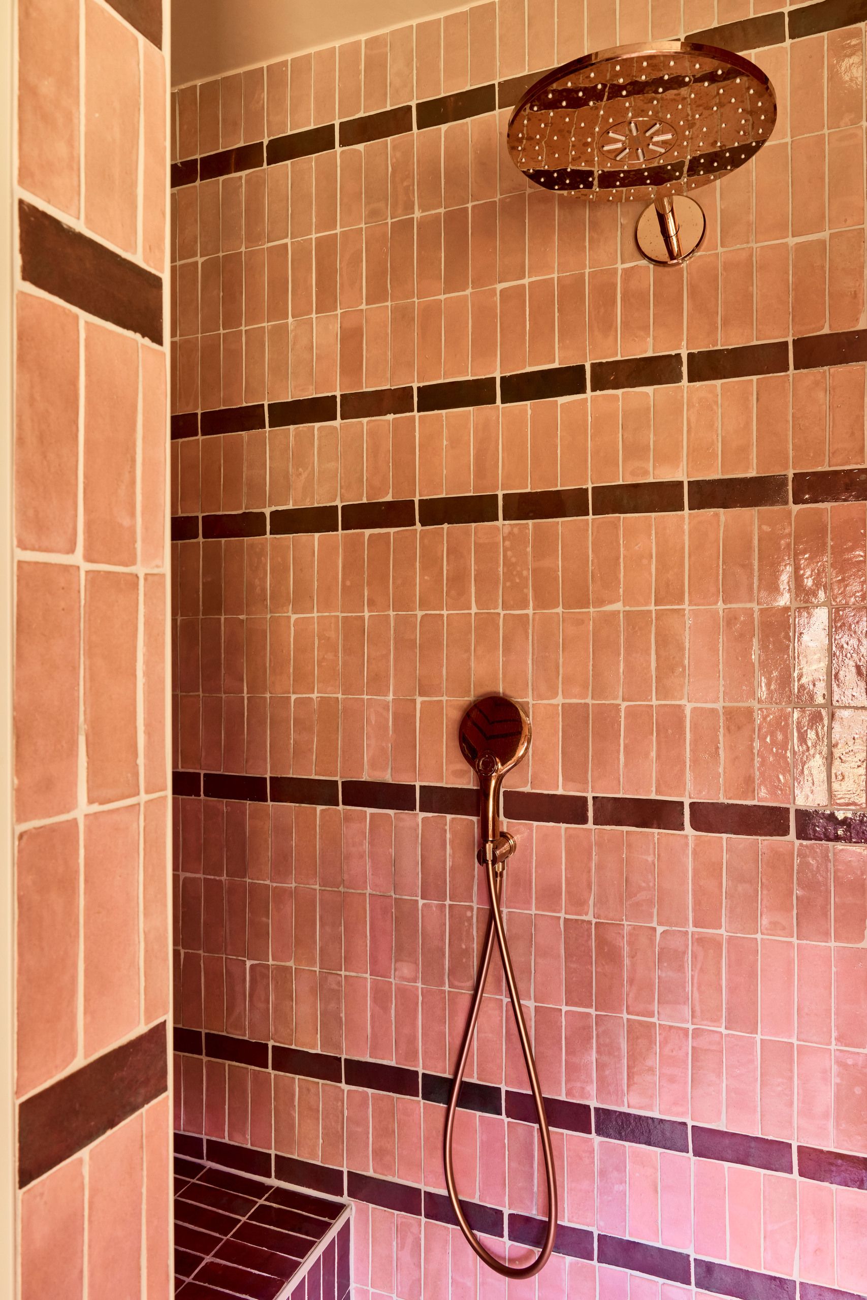 Close-up of a tile shower made out of pink and burgundy zeillege tiles.