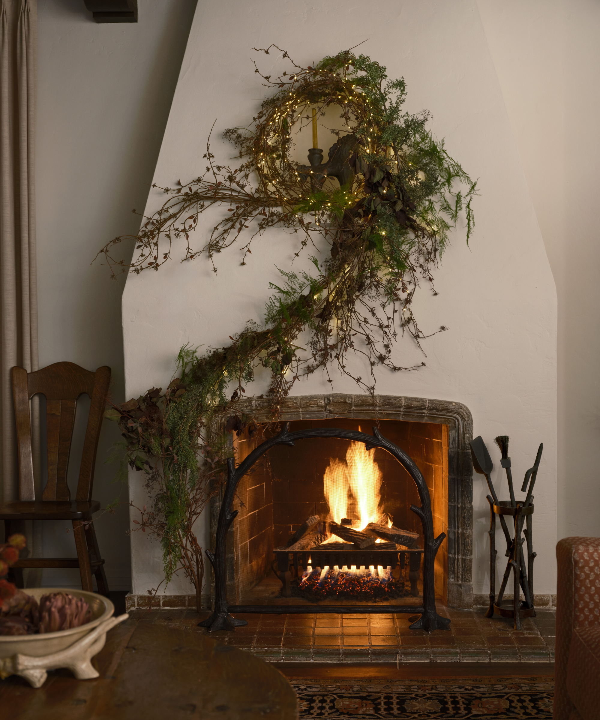 a fireplace with a glowing fire and a climbing vine-like garland trailing up the side and twisting in the center of the mantel
