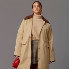 model wears trench coat, tan sweater, plaid skirt, shoes and red purse